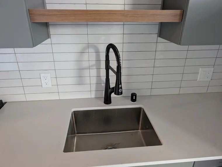 Commercial-style matte black spring faucet installed on Camano Island — stainless sink, white tile backsplash